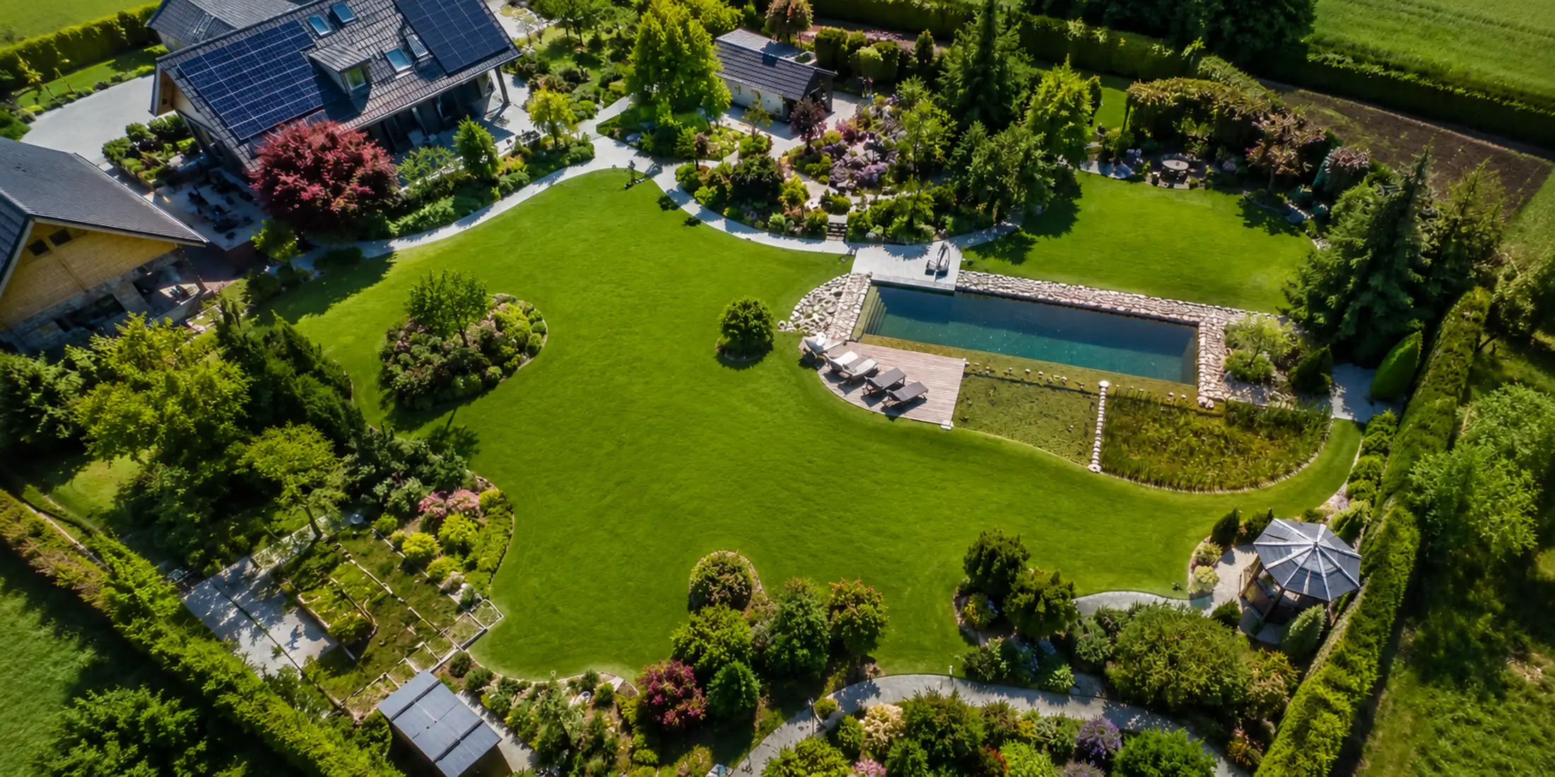Luftaufnahme eines traumhaft angelegten Gartens mit Naturpool und geschwungenen Wegen